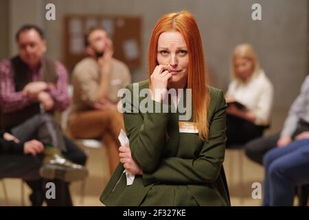 Unhappy and crying middle aged woman in casualwear looking at you while standing against several patients of mental support group Stock Photo