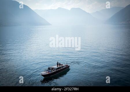Italy, Lombardy, Lenno, view of Lake Como from Villa del Balbianello, couple embracing on a wooden speedboat
