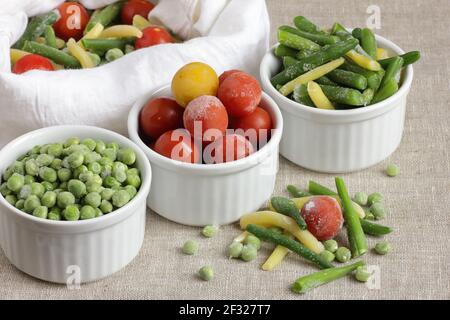 Frozen vegetables assorted in bowls isolated on white background, closeup, saving leftovers, food storage concept and eating meals at home concept Stock Photo