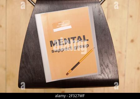 Overview of grey folder with notice saying mental support group and pencil lying on black wooden chair in front of camera Stock Photo