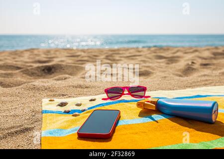 Towel, sunsreen, sunglasses and smart phone on the beach. Summer concept. Stock Photo
