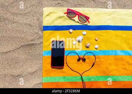 Towel, smart phone, sunglasses, headphones, sunscreen on the beach. Summer concept. Stock Photo