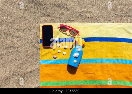 Towel, sunsreen, sunglasses and smart phone on the beach. Summer concept. Stock Photo