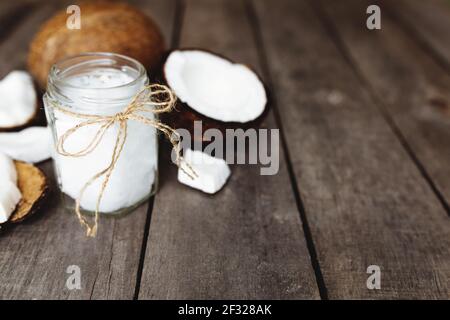 Broken coconuts on gray wooden background with jar of raw organic extra virgin coconut oil. White coconut pulp. High quality photo Stock Photo