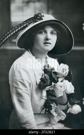 The notable Edwardian English stage, and later film, actress Gladys Cooper (1888-1971) wearing a hat and holding a bunch of roses, taken from a photographic postcard from the era. Stock Photo