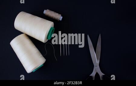 Sewing accessories on a black background. Sewing threads, needles, scissors. A top view, flatlay Stock Photo