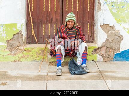Indigenous Tarabuco man in traditional clothing sitting in front of a wooden door, Tarabuco town, Sucre Department, Bolivia. Stock Photo
