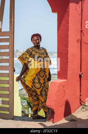 Africa Woman wearing yellow suit stands at a gate with background over the city of Accra in Ghana Stock Photo