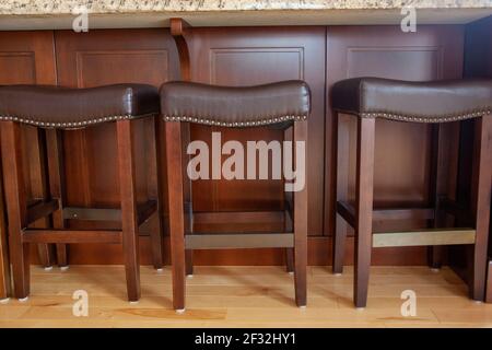 wooden legs and brown leather stools sitting against an island in the kitchen Stock Photo