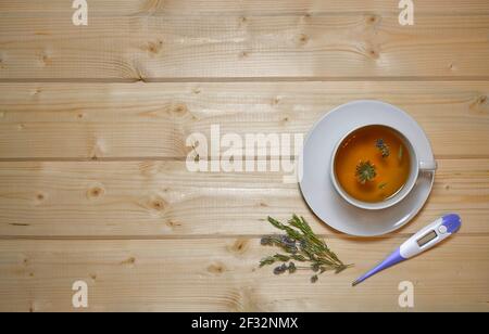 A cup and saucer of thyme herbal tea and a thermometer next to it. Flat lay on a wooden table top. Stock Photo