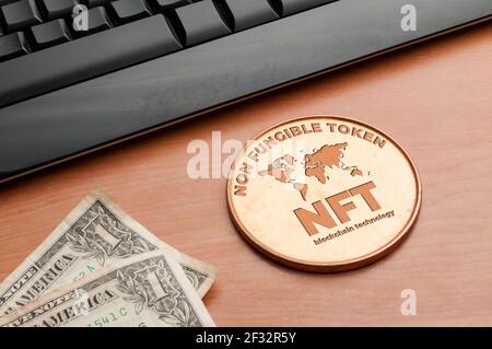 Nft (non fungible token) concept: big copper coin on a wooden table with a computer keyboard and two dollar bills Stock Photo