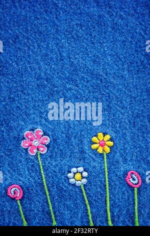 Embroidered 5 flowers on fragment of  blue denim jeans texture Stock Photo