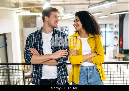 Portrait of successful stylish friends colleagues or students, smiling to each other. Happy young adult multiracial people are standing in modern office with cross hands, partnerships concept Stock Photo