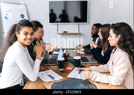 Successful group of business people at conference, discussing project. Multiracial employees in formal suits looking at financial graphs, brainstorming together, working on new startup Stock Photo