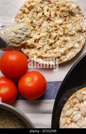 Crispy puffed rice cakes on table hummus spread and tomato vegetables and sesame seeds on the table - top view on healthy vegetarian or vegan breakfas Stock Photo