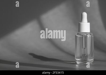 Glass cosmetic bottle with pipette, anti aging serum with collagen and peptides product packaging with shadows from sun on grey background, cosmetic Stock Photo