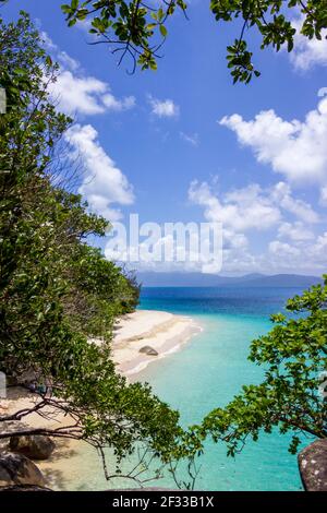 Queensland Australia the clear waters of the Coral Sea meet the warm sands of Nudey Beach on Fitzroy Island as seen between the jungle trees. Stock Photo