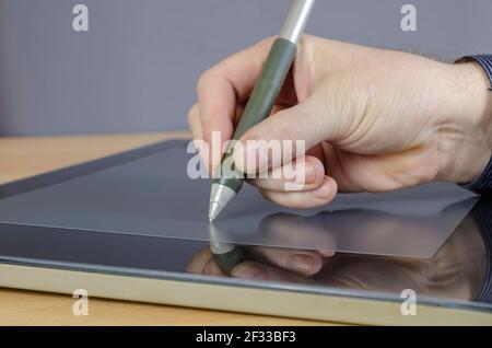 A designer's hand drawing with a special pen on the screen of a graphics tablet. A man's hand and a professional device for designers in close-up.  Si Stock Photo