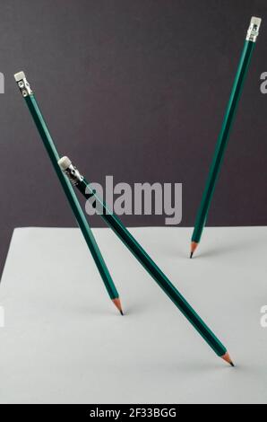 Blank sheet of paper and standing pencils on a gray background. Three green wooden pencils stand magically on a white sheet of office paper. Selective Stock Photo