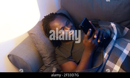 Happy young black man smiling while using smartphone. Connection during quarantine. High quality photo Stock Photo