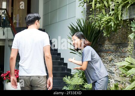 Smiling pretty Asian woman bowing to man entering spa salon building and doing inviting gesture Stock Photo