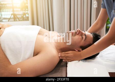 Calm handsome young man enjoying relaxing face, head and shoulders massage in spa salon Stock Photo