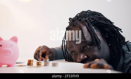 Desperate black man looking sad in the coins near the piggybank. High quality photo Stock Photo