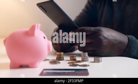 Man using phone to check his bank account. Piggy bank credit card and coins on the table. Investment using mobile app. High quality photo Stock Photo