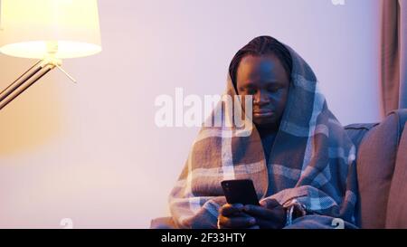 Young african american black man covered with blanket over the head using smartphone with smile. High quality photo Stock Photo