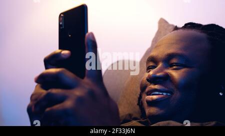 Man relaxing in the couch and browsing dating site on his smartphone. High quality photo Stock Photo