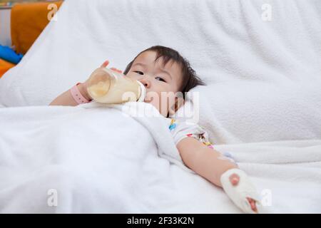 Little asian girl lying and suck up milk on a sickbed in hospital, saline intravenous (IV) on hand Stock Photo
