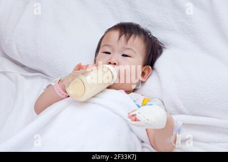 Little asian girl lying and suck up milk on a sickbed, saline intravenous (IV) on hand Stock Photo