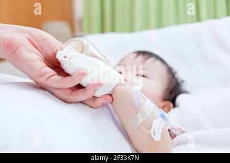 Woman holding baby hand, little asian girl lying and suck up milk on a sickbed, saline intravenous (IV) on hand, shallow depth of field (DOF) saline i Stock Photo