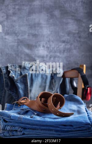 Denim jeans at old wooden chair and belt near grey wall background texture. Front view of classic jeans fashion Stock Photo