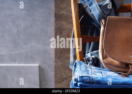 Denim jeans and old leather bag at wooden chair near grey wall background texture. Modern casual style of classic jeans fashion Stock Photo