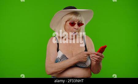 Senior woman tourist browsing on mobile phone app, looking for resort hotel on chroma key background Stock Photo