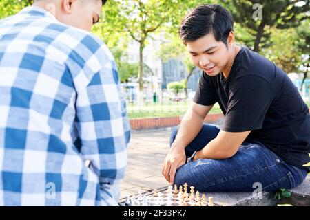 Two Asian guys sitting on bench on the street and playing chess together Stock Photo