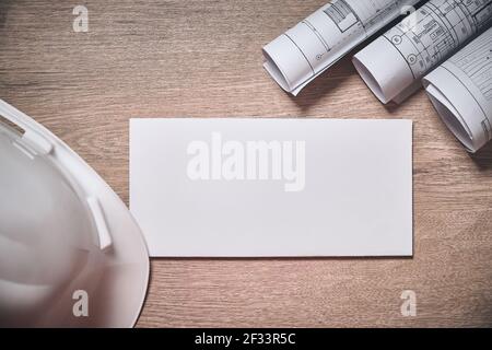 Engineer hardhat, rolled drawings and blank white envelope at wooden table Stock Photo