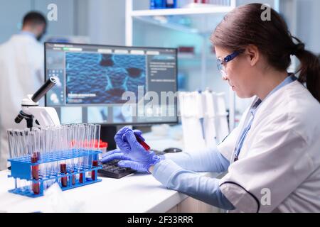 Professional scientist looking at analysis of blood tube for medical experiment. Medical woman chemist researcher analyzing test sample developing vaccine against covid19 Stock Photo