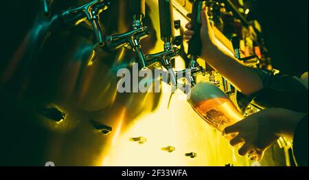 Hands of female barman pouring a cold lager beer from tap to glass in neon light Stock Photo