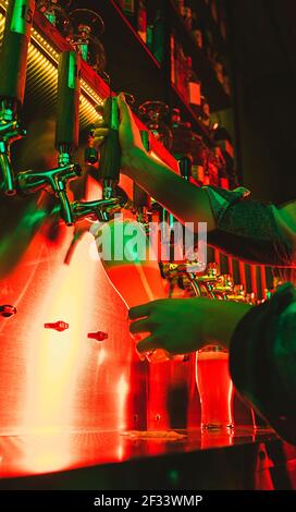 Hands of female barman pouring a cold lager beer from tap to glass in neon light Stock Photo