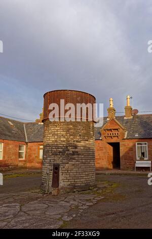 The Old Historical Iron Water Tower on a brick base in Fountain Square Aucmithie, with a small Doocot above the entrance of the central cottage, Stock Photo