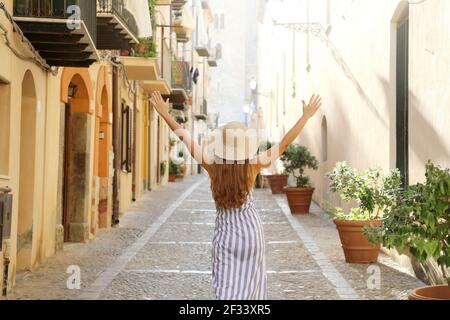 Europe travel vacation fun summer woman with arms up and hat happy in Cefalu, Italy. Carefree tourist girl in European destination walking in sunny al Stock Photo
