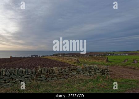 Looking over the Fields and Dykes of Farmland towards the old Coastal Village of Auchmithie with dark early morning clouds building. Stock Photo
