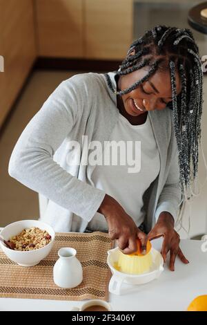 Happy pretty Black young woman using plastic juicer when making breakfast in kitchen Stock Photo