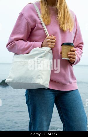 Young woman hold stylish eco bag and paper cup against sea Stock Photo