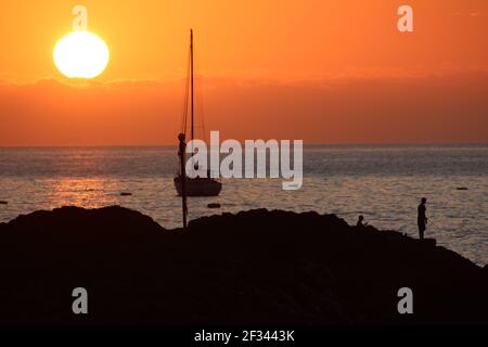 A man fishes from rocks as the sun sets over James Bay at Jamestown on the island of St Helena Stock Photo