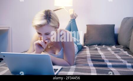 Young happy woman using a laptop in her bedroom. Browsing social media. High quality photo Stock Photo