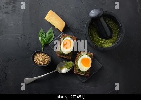 Fresh Green basil pesto homemade on old rustic wood eggs panini bread with pesto silver spoon on italian breakfast with ingredients green pesto on bla Stock Photo