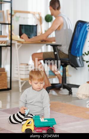 Child playing with toys with his father working on computer in the background at home Stock Photo